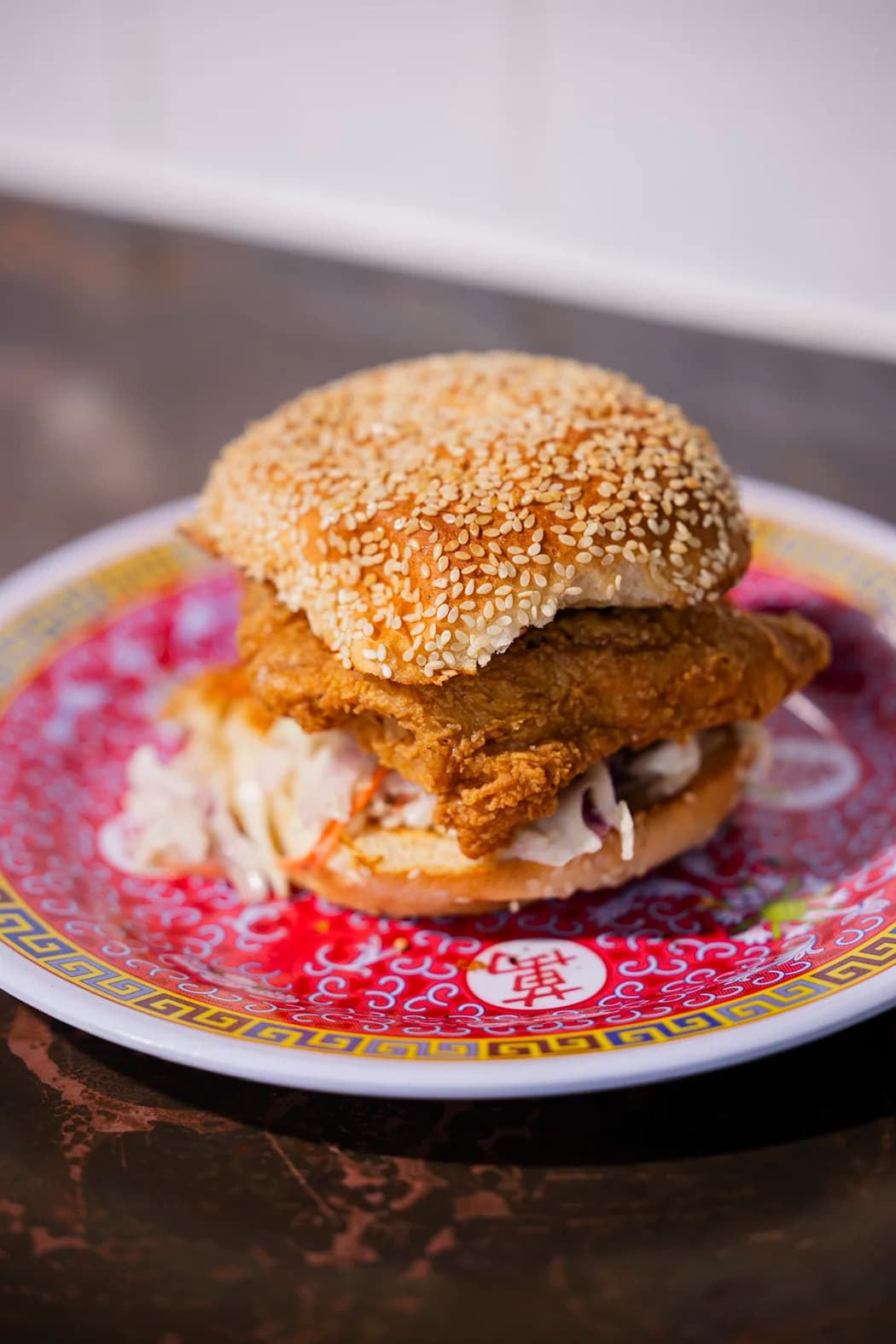 A fried fish sandwich on a red and yellow Chinese-patterned plate.
