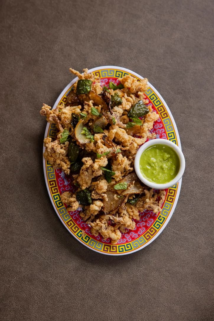 An overhead plate of salt-and-pepper bites with a green dipping sauce.